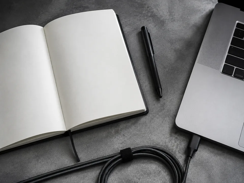 Notebook, pen, and laptop arranged on a gray worktable